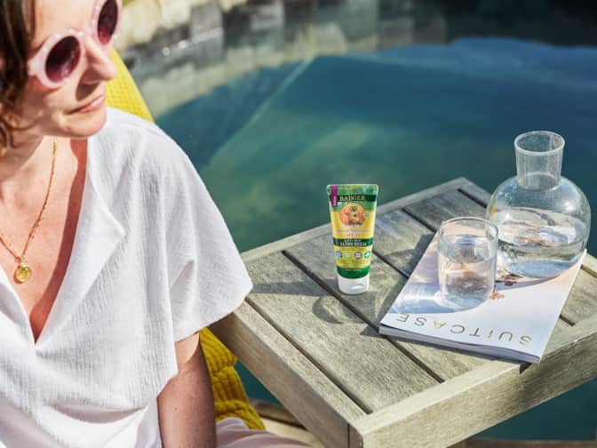 Woman with yellow sunglasses sitting by pool with Badger product on table 