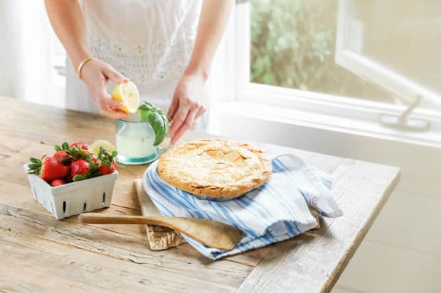 Image of fresh baked pie, container of strawberries, and someone juicing a lemon on countertop