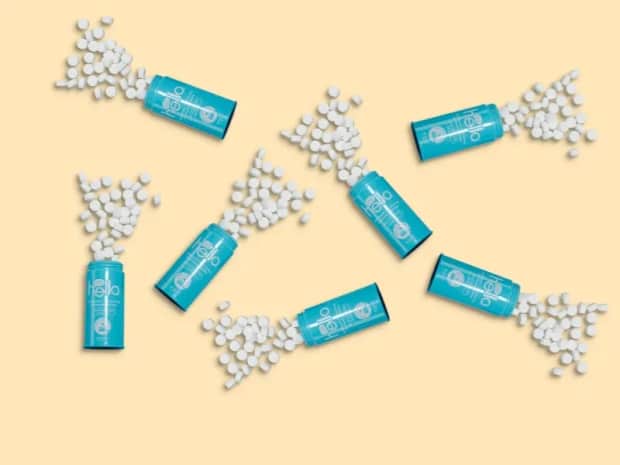 toothpaste tablet containers with tablets spilling out on a pale yellow background
