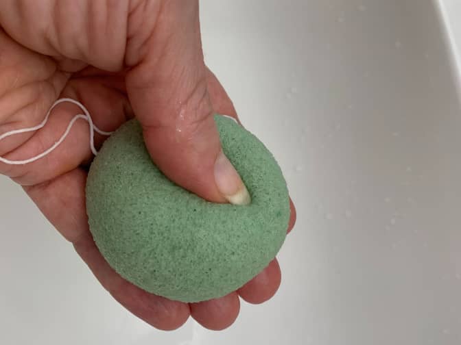 Image of hand holding green konjac sponge under running water in sink