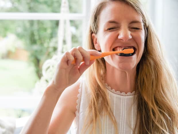 woman brushing her teeth with charcoal toothpaste