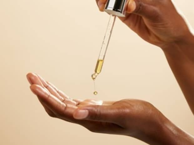 Hands applying serum from eye dropper