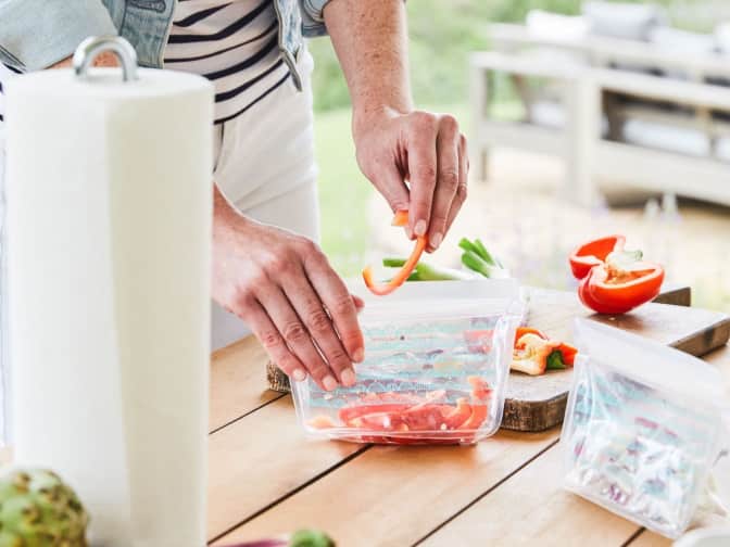 Woman placing sliced red bell peppers into a reusable zipper sealed bag