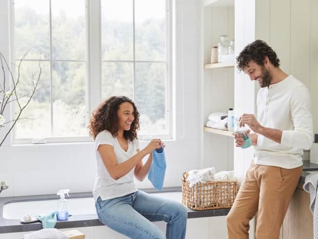 young biracial couple smiling in a bathroom holding cleaning products